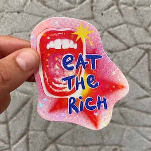 Peut inclure: Un autocollant découpé à la forme avec une finition holographique représentant une bouche ouverte rouge et le texte bleu EAT THE RICH. Le design comprend des étoiles jaunes et un effet de fond peint à la bombe rose et rouge sur une bordure blanche.