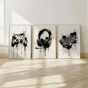 Könnte beinhalten: Ein Set aus drei gerahmten Wandbildern mit schwarz-weißen Aquarell-Illustrationen von Gaming-Ausrüstung. Die Bilder zeigen einen Videospiel-Controller, einen Gaming-Kopfhörer mit Mikrofon und eine mechanische Computertastatur.