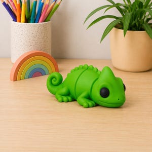 Könnte beinhalten: Eine leuchtend grüne Chamäleon-Figur mit glatter, matter Oberfläche, die einen geringelten Schwanz und große schwarze Augen aufweist. Die Eidechse ist in horizontaler Haltung positioniert und zeigt einen segmentierten Körper mit sichtbaren Rückenleisten.