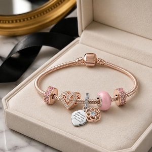 Pode incluir: Uma pulseira de corrente de cobra em ouro rosa com dois espaçadores cravejados de cristais cor-de-rosa, um berloque em forma de coração, uma conta rosa lisa e dois berloques pendentes, um deles em forma de nuvem com a gravação "Moments spent with you are my favourite."