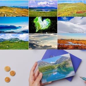 以下が含まれることがあります： 山、森、湖を写した9枚の風景写真のコラージュと、青い封筒の上に置かれた1枚のポストカード。左側には、エンボス加工が施された3つの小さな丸い茶色の木製トークンが配置されています。