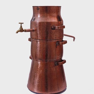 May include: A three-tiered hammered copper vessel featuring a brass spigot on the upper section and two side handles on each tier. The structure is cylindrical with a tapered top and base, showcasing a metallic finish and visible rivets.