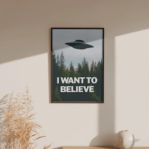 May include: A rectangular wall poster in a dark frame featuring a dark gray flying saucer hovering above a dense green forest of pine trees. The text I WANT TO BELIEVE is printed in bold white capital letters across the lower portion of the image.
