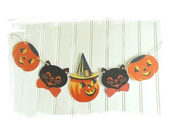 May include: A Halloween garland featuring five paper cutouts strung together. The design includes two orange jack-o'-lanterns, two black cats with orange bow ties, and a central orange jack-o'-lantern wearing a black and yellow witch hat.