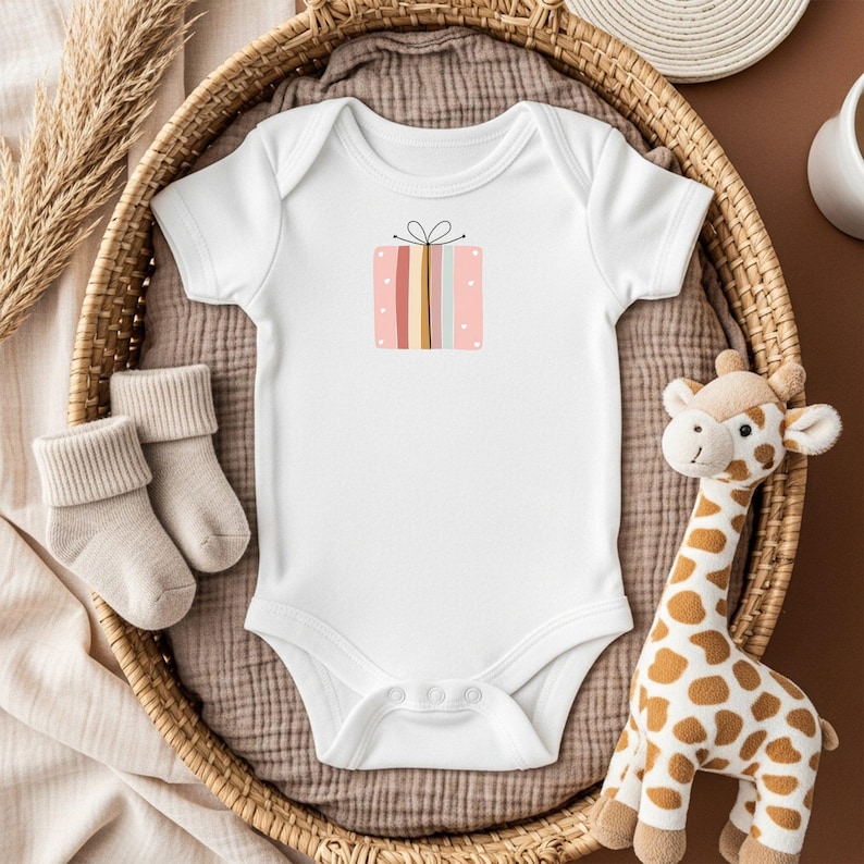 May include: White baby onesie with a colorful gift box graphic. The onesie is placed in a woven basket with a pair of beige baby socks and a stuffed giraffe toy. The gift box design features pink, yellow, and blue stripes.