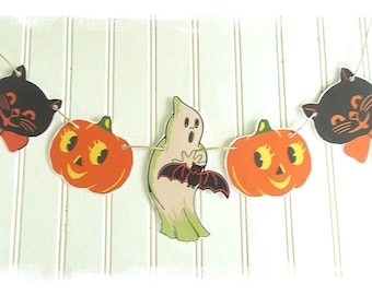 Może przedstawiać: Girlanda o tematyce Halloween z wyciętymi kształtami czarnych kotów z pomarańczowymi kokardkami, pomarańczowymi dyniami i zielonym duchem trzymającym nietoperza. Kształty są połączone sznurkiem.