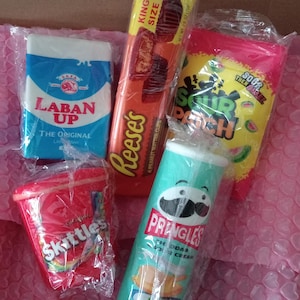 May include: A collection of five individually wrapped snack items including a blue Laban Up drink carton, a yellow Reese's King Size peanut butter cups package, a pink Sour Patch Kids bag, a red Skittles cup, and a green Pringles Cheddar Sour Cream can.
