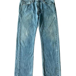 Könnte beinhalten: Eine hellblaue Jeans aus Denim mit klassischem Fünf-Taschen-Design, Knopfleiste und geradem Beinschnitt. Der Stoff zeigt eine helle Waschung mit dezenten Abnutzungsspuren an den Oberschenkeln und einen standardmäßigen Hosenbund.