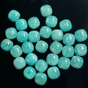 Könnte beinhalten: Eine Sammlung loser, polierter, quadratischer Amazonit-Edelsteine mit abgerundeten Ecken. Jeder Stein zeigt eine lebendige, undurchsichtige türkis-grüne Farbe mit feiner, natürlicher weißer Maserung und einer glatten, reflektierenden Oberfläche.