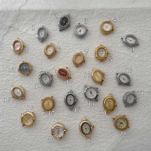 May include: A collection of twenty-four small analogue watch faces in various gold and silver tones, each labelled with a number from 1 to 24. The watch faces feature diverse designs, including round and oval shapes, different dial colours, and textures.