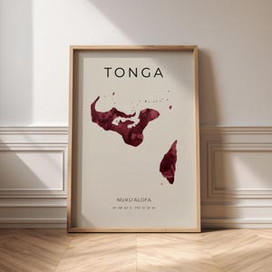 May include: A framed wall art print featuring a map of Tonga in deep red watercolour texture on a light beige background. The text reads TONGA at the top, and NUKU'ALOFA with the coordinates 21° 08' 22" S 175° 12' 12" W at the bottom.