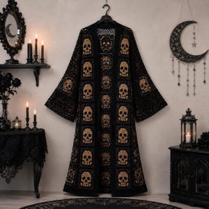 May include: A long, open-front crochet cardigan featuring a repeating pattern of tan skull motifs set within black square panels. The garment has wide, flared sleeves and a full-length silhouette, constructed from intricate black yarn work.