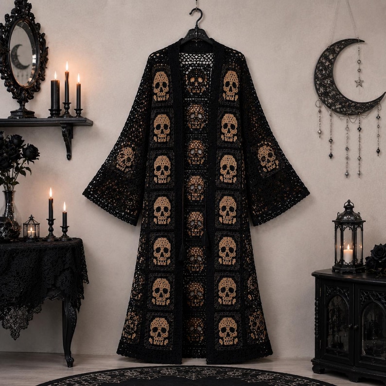 May include: A long, open-front crochet cardigan featuring a repeating pattern of tan skull motifs set within black square panels. The garment has wide, flared sleeves and a full-length silhouette, constructed from intricate black yarn work.