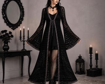 May include: A long, black, open-front crochet duster cardigan featuring wide, flared bell sleeves and a delicate grey lace trim along the edges. The garment includes a thin tie closure at the chest and is worn over a simple black mini dress.