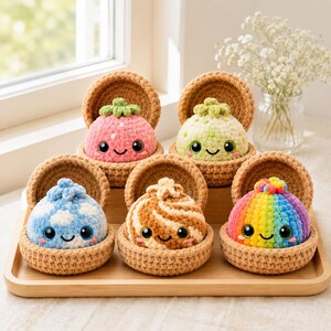 Puede incluir: Cinco pequeños juguetes de peluche tejidos a ganchillo, redondos, con caras sonrientes y grandes ojos negros, cada uno en un cuenco de ganchillo color canela. Los juguetes presentan varios diseños: una fresa rosa, un cactus verde claro, una nube azul, un remolino marrón y un arcoíris.