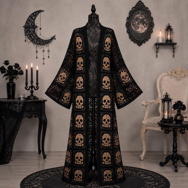 May include: A long, open-front cardigan made of black crochet squares, each featuring a tan skull motif. The garment has wide, flared sleeves and a floor-length silhouette, constructed from a repeating pattern of individual square panels.