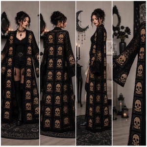 May include: A long, open-front cardigan made of black crochet squares, each featuring a tan skull motif. The garment has long, wide sleeves and a floor-length hem, constructed from a repeating pattern of skull-detailed squares throughout the entire piece.