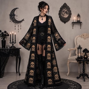 May include: A long, open-front black crochet duster cardigan featuring a repeating pattern of tan-coloured skull motifs. The garment has wide, flowing sleeves and a floor-length hem, constructed from square crochet panels that showcase intricate detail.
