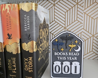 May include: A dark gray arched tracker sign with the text BOOKS READ THIS YEAR and three rotatable number dials. The sign features decorative cutouts of three dragons, a crescent moon, and four-pointed stars in black, blue, and gold colors.