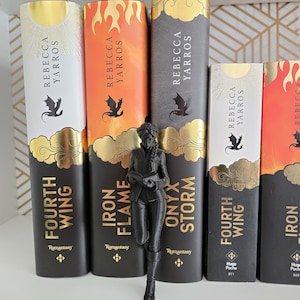 May include: A black 3D-printed figurine of a person reading a book stands in front of five books by Rebecca Yarros. The books are titled Fourth Wing, Iron Flame, and Onyx Storm, featuring black, white, orange, and gold foil cover designs.