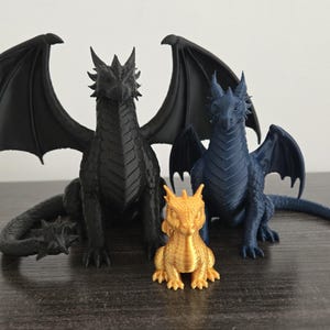 May include: Three dragon figurines in different sizes and colors. A large black dragon with spread wings, a medium-sized dark blue dragon with folded wings, and a small gold dragon sitting in the front, all featuring detailed scales and horns.