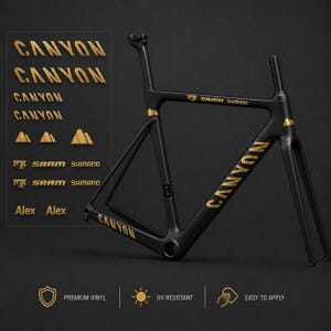 Könnte beinhalten: Ein mattschwarzer Fahrradrahmen mit goldfarbenen Aufklebern, darunter der Schriftzug CANYON, SRAM, SHIMANO, FOX und Alex sowie Bergsymbole. Das Set enthält mehrere Aufklebervarianten, die als Premium-Vinyl, UV-beständig und einfach anzubringen gekennzeichnet sind.