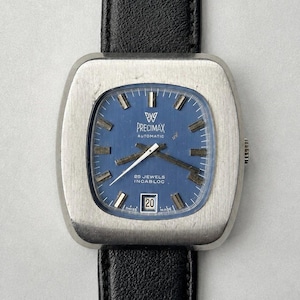 May include: A Precimax automatic wristwatch with a square silver-tone case and a blue dial. The watch features silver hour markers, a date window at the six o'clock position displaying the number 20, and a black leather strap with a textured finish.
