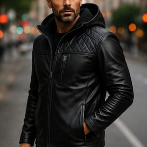 May include: A black hooded jacket featuring a quilted diamond pattern across the upper chest and shoulders. The jacket includes a full-length front zip, a vertical zipped chest pocket, and two side pockets. It is worn over a black shirt.