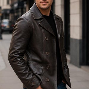 May include: A dark brown leather double-breasted jacket featuring a wide notched collar, long sleeves with buttoned cuffs, and two front flap pockets. The jacket is worn over a black shirt and blue denim jeans, showcasing a structured fit.