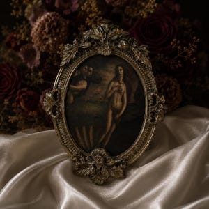 May include: An oval-shaped picture frame with an ornate, antique gold finish featuring intricate leaf and scroll detailing. The frame holds a dark-toned print depicting a figure standing in a shell-like structure with other figures in the background.