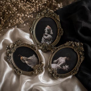 Pode incluir: Três molduras ovais com bordas de metal dourado antigo ornamentadas, apresentando detalhes em relevo de folhas e flores. Cada moldura contém um retrato de tons escuros de uma figura vestindo um vestido histórico branco.