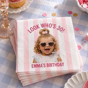 Puede incluir: Una pila de servilletas de papel cuadradas con un patrón de rayas verticales rosas y blancas. El centro muestra una fotografía de un niño con gafas de sol en forma de corazón, con el texto LOOK WHO'S 30! arriba y EMMA'S BIRTHDAY abajo.