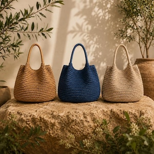 May include: Three structured handbags with rounded handles and a textured, woven exterior. The bags are arranged in a row, featuring a tan bag on the left, a deep navy blue bag in the centre, and a light beige bag on the right side.