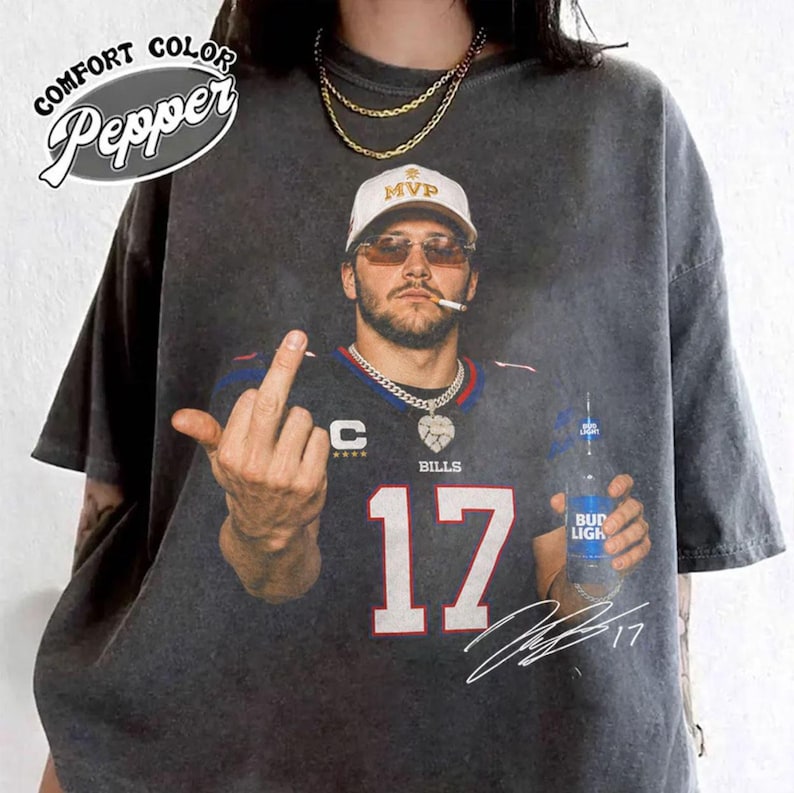 May include: A charcoal gray t-shirt featuring a graphic of a person wearing a white MVP cap, sunglasses, and a dark blue jersey with the number 17. The person is holding a Bud Light bottle and giving the middle finger. Includes a signature and text.