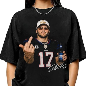 May include: A black t-shirt featuring a graphic of a person wearing a white MVP cap, sunglasses, and a black football jersey with the number 17. The person is holding a Bud Light bottle and giving the middle finger. A white signature is printed below.