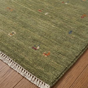 May include: A sage green area rug featuring a textured pile surface with small, scattered geometric and animal-like motifs in red, blue, orange, and white. The rug is finished with a short, white knotted fringe along the bottom edge.