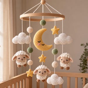 Puede incluir: Un móvil colgante para cuna con elementos de ganchillo suspendidos de un marco circular de madera. El móvil incluye una luna creciente amarilla, tres ovejas blancas, tres estrellas amarillas, nubes blancas y pequeñas esferas verdes y crema.