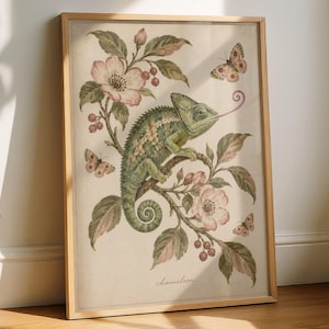 Könnte beinhalten: Ein gerahmter Druck im botanischen Stil zeigt ein grünes Chamäleon auf einem blühenden Zweig mit rosa Blüten und Beeren. Drei Schmetterlinge sind um das Chamäleon herum abgebildet, das seine Zunge herausstreckt. Unten steht das Wort chameleon.