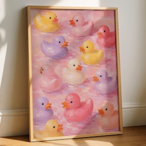 Peut inclure: Une impression d'art encadrée représentant une illustration de style peinture à l'huile de plusieurs canards en caoutchouc de diverses couleurs pastel, dont jaune, rose, violet et blanc, flottant sur un fond d'eau rose texturé.