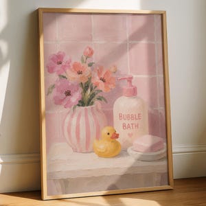 Peut inclure: Une peinture encadrée représentant une scène de salle de bain avec un vase rayé rose et blanc rempli de fleurs roses et orange, une bouteille étiquetée BUBBLE BATH, un canard en plastique jaune et un savon rose sur une surface blanche.