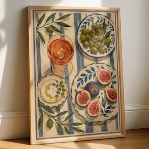 Könnte beinhalten: Ein gerahmter vertikaler Kunstdruck mit einer Draufsicht auf einen Tisch mit blauen und weißen Streifen. Die Szene zeigt ein Glas mit bernsteinfarbener Flüssigkeit und Eis, eine Schale mit grünen Oliven, einen Teller mit Feigen und Käse.