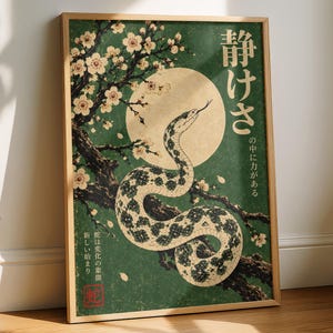 Peut inclure: Une affiche murale verticale encadrée présentant un fond vert avec un serpent enroulé, une grande lune pâle et des branches d'arbre en fleurs. L'œuvre comprend des caractères japonais et un sceau carré rouge, dans un cadre en bois clair.