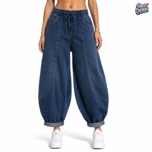 Peut inclure: Pantalon en jean bleu foncé avec une taille élastique haute et un cordon de serrage. Ce pantalon large présente des coutures verticales marquées, des poches latérales et des ourlets à revers. Le texte Street Override apparaît en haut.