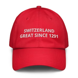 May include: A bright red baseball cap featuring white embroidered text on the front panel that reads SWITZERLAND GREAT SINCE 1291. The cap has a structured crown, a curved brim, and a button at the top center, showcasing a clean design.