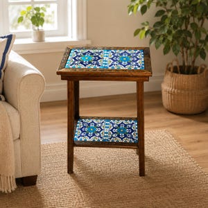 May include: A rectangular wooden side table featuring four decorative ceramic tiles with a blue, white, and yellow floral pattern. The table has a dark brown wood frame with a lower shelf that also contains two matching patterned ceramic tiles.