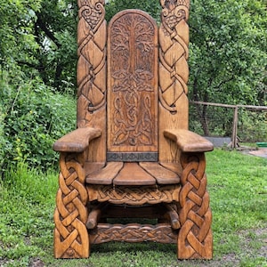 May include: A tall, brown wooden chair featuring intricate hand-carved details. The backrest displays a central tree motif surrounded by Celtic knotwork. The armrests and legs are adorned with braided wood carvings, and a row of runic symbols is carved into the horizontal panel just below the backrest.