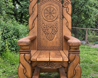 May include: A tall wooden chair featuring intricate carvings of two dragon heads at the top, a central circular symbol, and elaborate knotwork patterns. The chair has sturdy armrests and a flat seat, all finished in a warm brown wood tone.