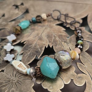 Puede incluir: Pulsera artesanal con cuentas turquesas, crema y plateadas. Incluye una gran piedra turquesa, cuentas en forma de flor y un cierre decorativo. La pulsera está hecha con varias cuentas.