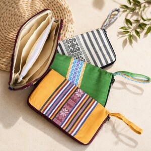 May include: Three rectangular zippered pouches with wrist straps. One is open, showing a cream interior with multiple compartments. The others are closed, featuring a black and white striped pattern, a solid green fabric, and a solid yellow fabric.