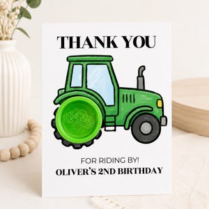 May include: A white rectangular card featuring a green tractor illustration with a bright green Play-Doh container as the rear wheel. The text reads THANK YOU, FOR RIDING BY!, and OLIVER'S 2ND BIRTHDAY in black capital letters.